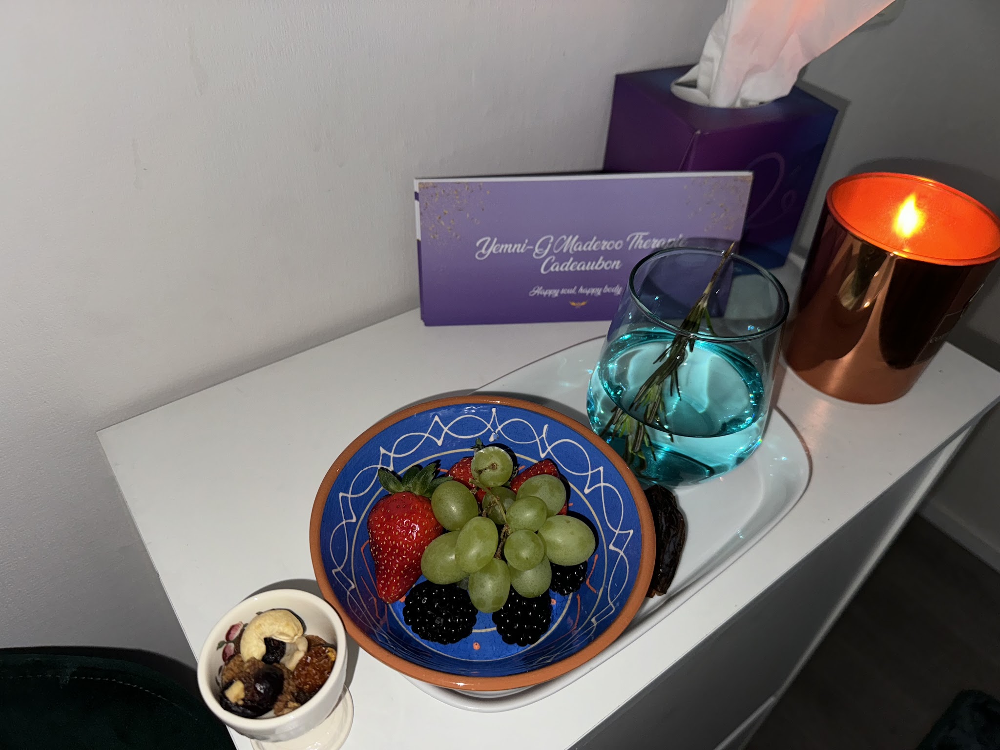 Een schaal met druiven, aardbeien en bramen naast een brandende kaars en een paarse cadeaubon