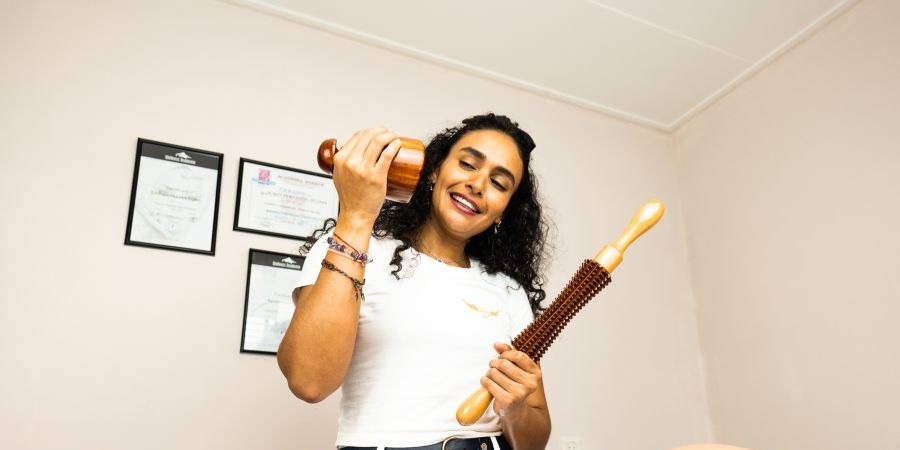 Yemni lachend met twee houten Madero-tools, met haar diploma’s aan de muur